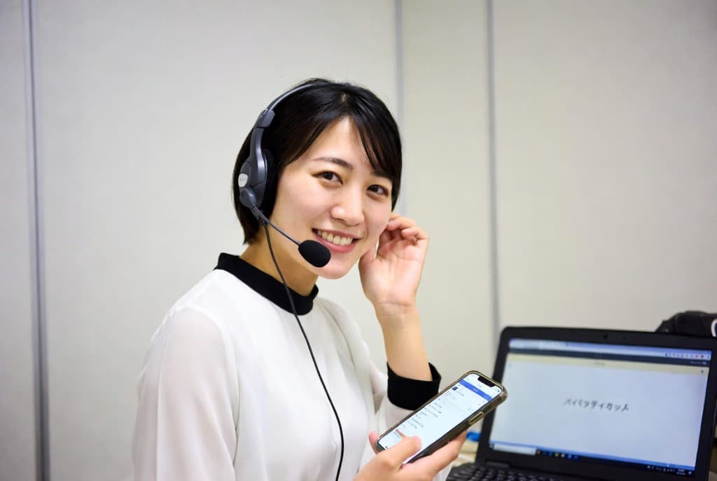 ヘッドセットを装着しスマートフォンを手に笑顔で対応する女性スタッフ